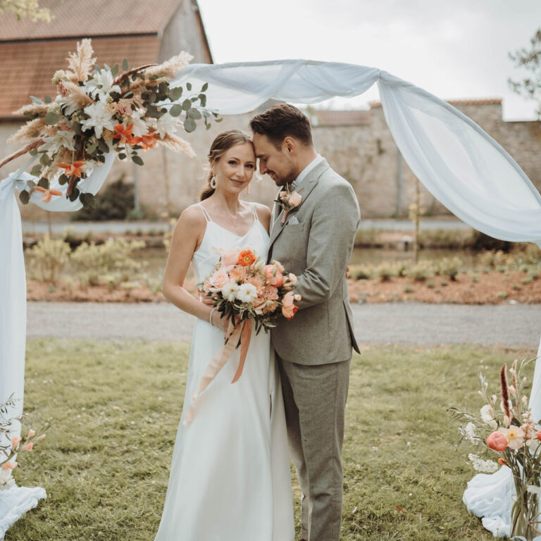 Hochzeitspaar steht vor dekorativem Traubogen, Blumendeko, Gutshof Rethmar